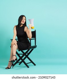 Black director chair.Asian woman is holding megaphone and sitting on chair. Mint green background.	