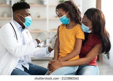 Black Doctor Making Vaccination Against Coronavirus In Shoulder For Teen Girl, African American Family In Protective Face Masks Visiting Pediatrician At Clinic. Kids Immunization Concept