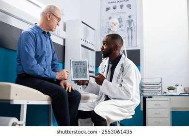 Black doctor uses tablet to explain diagnosis to older white man during checkup. Senior patient engages attentively as african american physician reviews treatment options using device for visual aid. - Powered by Shutterstock