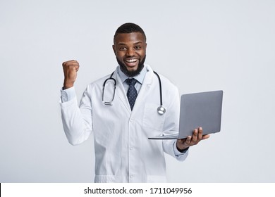 Black Doctor In White Robe With Laptop Exclaiming Happiness Over White Background