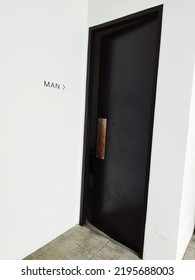 Black Door, Entrance Of Male Toilet. Public Restroom With Male Toilet Sign On White Wall.