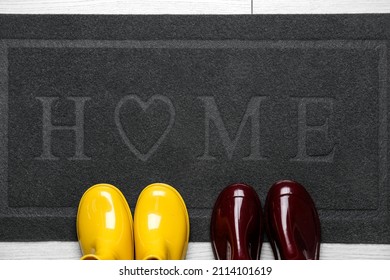 Black Door Mat With Gumboots On White Wooden Floor, Closeup