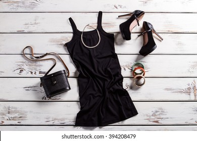 Black dress, shoes and jewelry. Black female outfit on table. Glamorous dark clothes with purse. Retro purse and modern clothing.