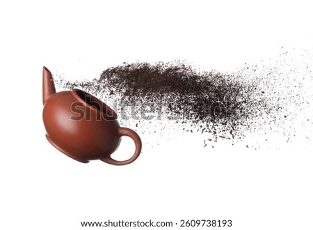 Black dried leave Tea fly on pot. Small Fine size tea leaf flying explosion, Abstract cloud fly. Brown colored Teas splash throwing in Air with tea pot. White background Isolated high speed freeze