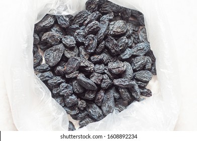 Black dried raisins in a plastic bag on a white table. The rate of dried blue grapes for an adult. Dried fruits