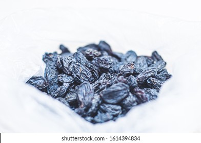 Black dried raisins in a plastic bag on a white table. The rate of dried blue grapes for an adult. Dried fruits