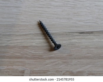 A Black Drywall Screw On A Wooden Background