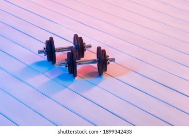 Black Dumbells On Wooden Floor With Red Neon Light. Equipment For Fitness At Home. Interactive Coach Concept