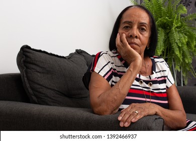 Black Elderly Woman On Sofa With Hand On Chin.