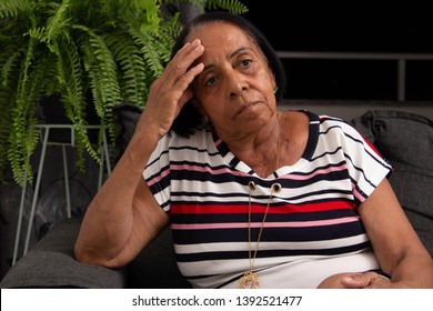 Black Elderly Woman Sitting On Sofa With Hand On Head.