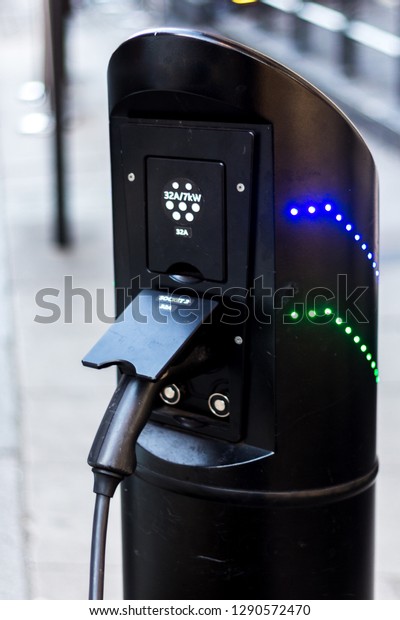 Black electric car charging station with blue\
and green leds and cable plugged\
in