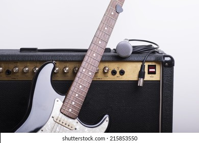 Black electric guitar, amp and mic on white background
