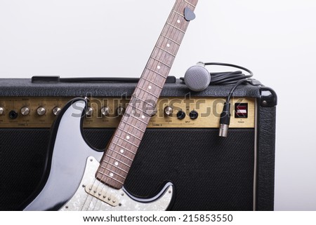 Black electric guitar, amp and mic on white background