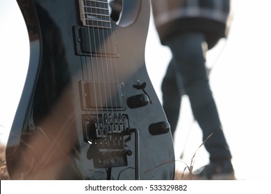 Black Electric Guitar With Person Walking Behind In The Background. Concept: Heavy Metal, Emo, Rock, Music