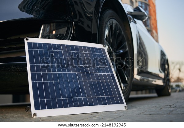 Black electric vehicle\
and photovoltaic solar panel on city street. Concept environmental\
innovational photovoltaic energy as alternative to automotive\
fuel.
