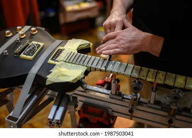 Black electrical guitar in repair service shop with a hands of a guitar luthier which fixes and tightens it