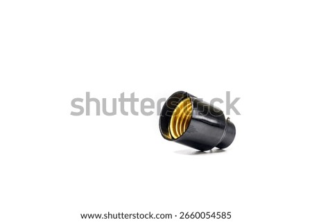 A black electrical light bulb socket, featuring a shiny golden threaded interior, is positioned at an angle against a clean white background.