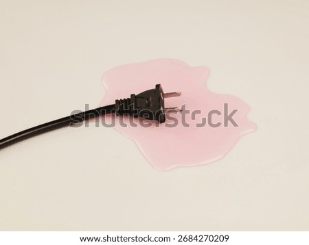 A black electrical plug immersed in a puddle of liquid on a light-colored surface.