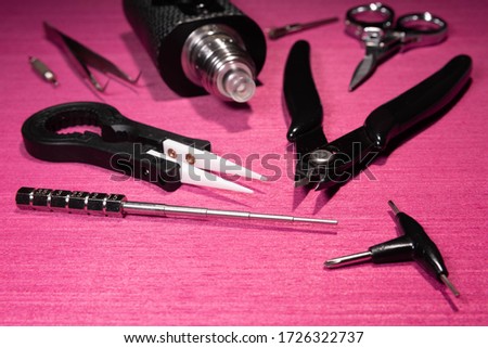 black electronic cigarette and various tools on pink table
