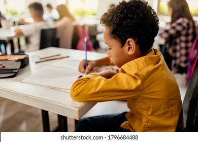 Black Elementary Student Writing On The Paper While Having Exam In The Classroom.