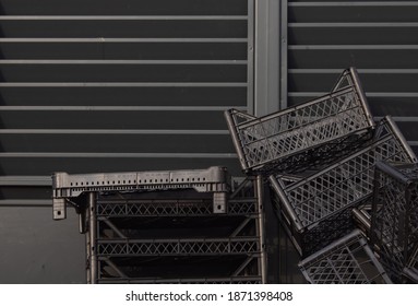 Black Empty Boxes After The Shipment Of Goods Are Stacked Against The Background Of A Black Plywood Fence During The Day