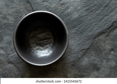 Black Empty Ceramic Bowl Isolated On Dark Grey Slate From Above. Space For Text.