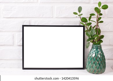 Un cadre noir vide se moque avec un espace de copie et plante dans un vase vert près d'un mur blanc de brique.  Orientation du paysage.