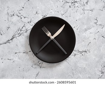 Black empty plate with crossed fork and knife on gray marble table, representing minimalist dining concept. Weight loss and dieting concept. - Powered by Shutterstock - Get 15% off with code: PIKWIZARD15
