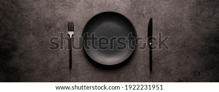 black empty plate and cutlery, fork and knife, on a dark textured background. Mockup concept for the design of a restaurant menu, website or design. long panoramic layout, central composition