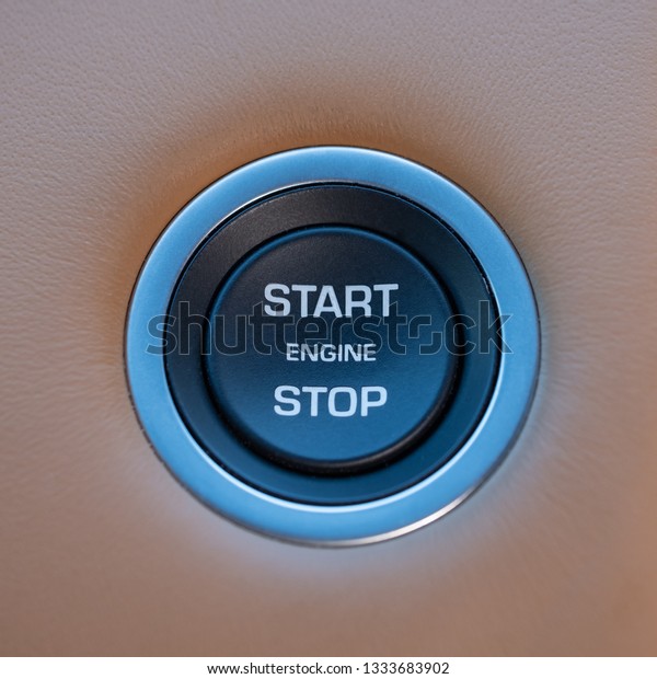 Black\
engine start stop button on tan leather\
dashboard.