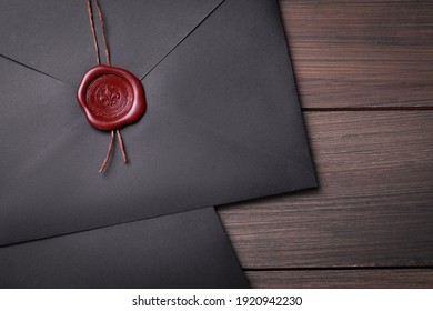 Black envelopes with wax seal on wooden background, flat lay