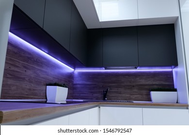 black ergonomic cupboards decorated with amazing violet neon strip light above wooden kitchen set surface