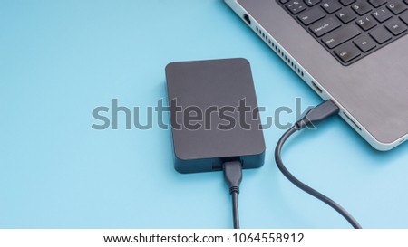 Black external hard disk connecting to a laptop on a blue background.