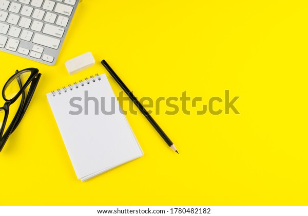 Black eye glasses, pencil, laptop, notepad planner and\
erase rubber on yellow background. Flat lay. Copy space. Workplace\
in the office. 