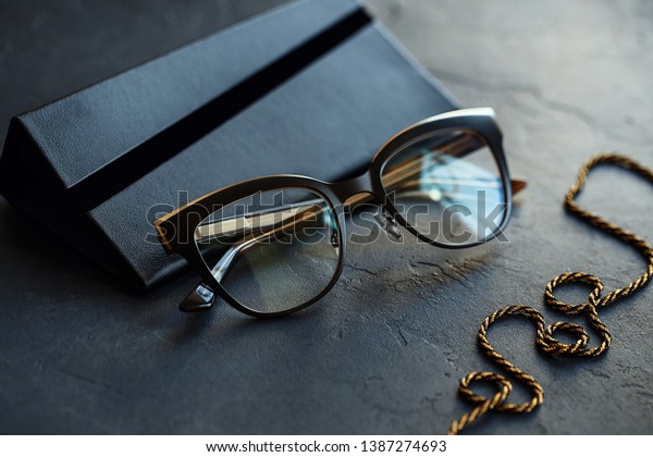 Black eyeglasses with\
transparent lenses and black case on dark concrete background.\
Close up view