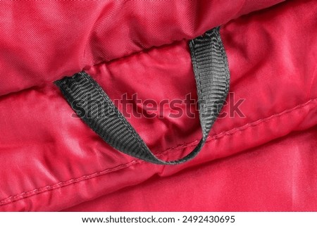 Black fabric jacket hanging loop on red waterproof fabric closeup as a background