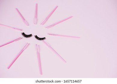 Black fake ribbon eyelashes and brushes for combing extension eyelashes on a pink trendy pastel background. False eyelashes, applicator and brushes. Top view, flat lay.