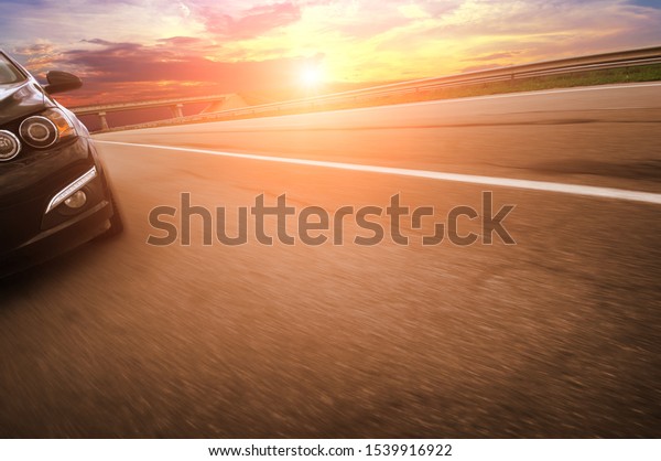 Black family car\
driving fast on the countryside asphalt road with a bridge against\
a night sky with a sunset