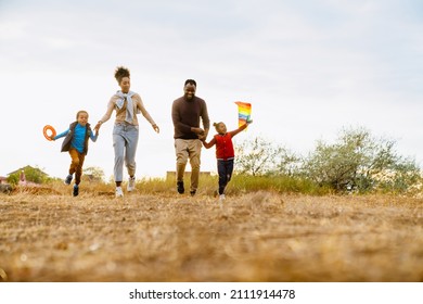 Black Family Laughing And Flying Kite While Running Together Outdoors