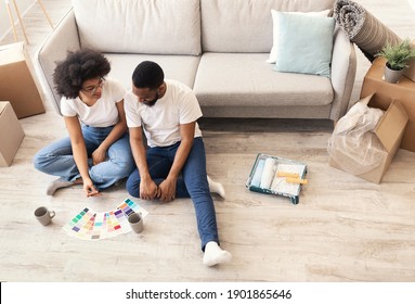 Black Family Planning Renovation And Wall Painting Choosing Color Palettes Together Sitting On Floor In New House After Moving In. Home Relocation And Living Room Interior Design. High-Angle View