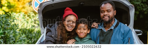 Black family smiling and hugging while sitting\
in trunk outdoors
