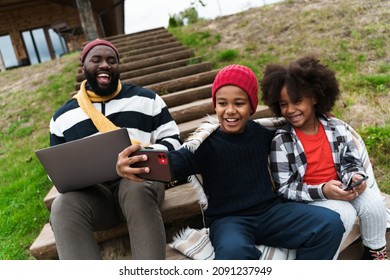 Black Family Taking Selfie On Cellphone And Using Cellphone While Resting Outside City