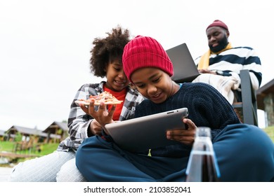 Black Family Using Gadgets And Eating Pizza While Resting Outside City