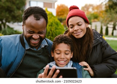 Black Family Using Tablet Computer While Resting Together On Backyard Outdoors