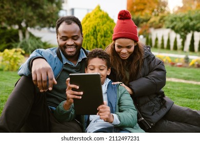 Black Family Using Tablet Computer While Resting Together On Backyard Outdoors