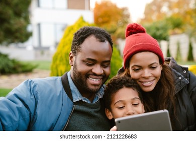 Black Family Using Tablet Computer While Resting Together On Backyard Outdoors