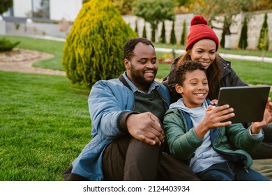 Black Family Using Tablet Computer While Resting Together On Backyard Outdoors