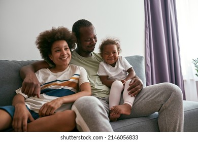 Black family watching TV or movie on sofa at home. Father hugging his daughter and son. Family relationship and enjoying time together. Fatherhood and parenting. Domestic entertainment and leisure