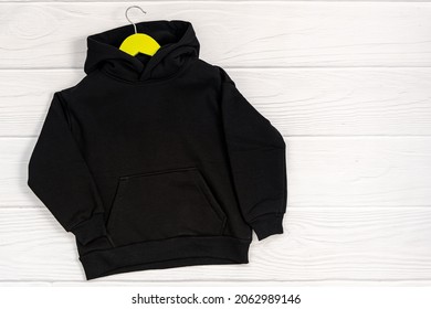 Black fashionable kid sweatshirt with a hood with clothes hanger on white background top view. Fashionable unisex clothing, hoodie, casual youth style, sports. Blank hoody mock up