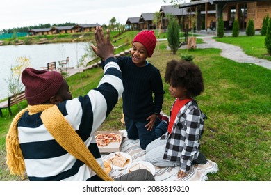 Black father and his sons giving high five and eating pizza while resting outside city - Powered by Shutterstock